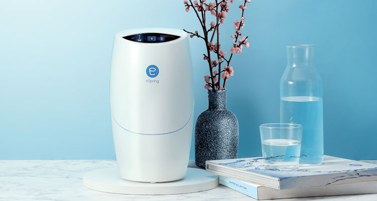 eSpring Water Treatment System against a blue backdrop beside books and a bottle of water