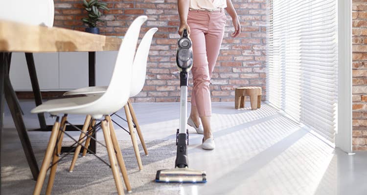 Lifestyle image of a woman vacuuming with the Philips SpeedPro Max Aqua Cordless Stick Vacuum Cleaner FC6903 