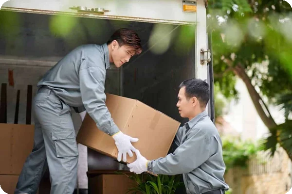 two movers in gray coveralls load a truck with boxes