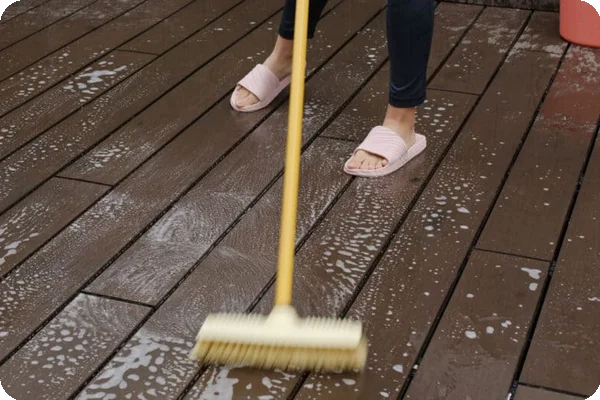 a person scrubs a wooden floor with a long-handled brush, water, and cleaner