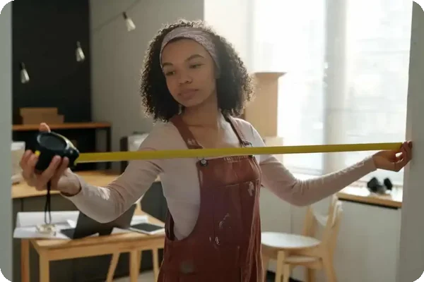 a woman uses a yellow measuring tape to measure a doorway's width