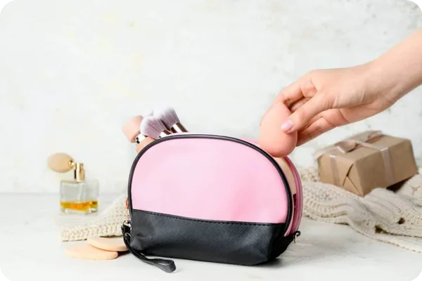 someone puts a pink makeup sponge into a bag filled with makeup brushes