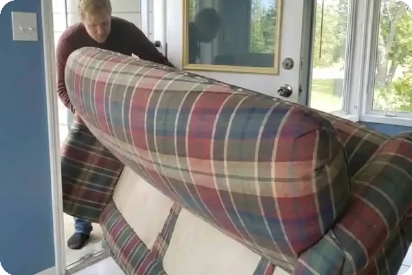a man pivots a plaid couch through a door