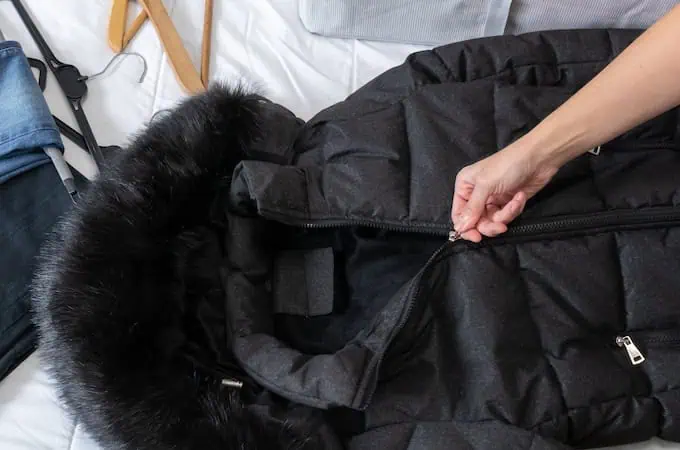 A black winter jacket being zipped up in preparation for it to be packed in a bag