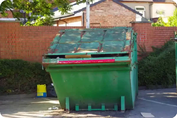 A green dumpster is sitting in front of a brick wall.