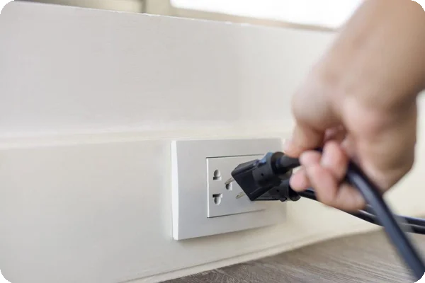 A person unplugs a black cord from a wall socket