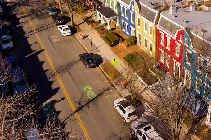 A view of colorful houses lining a Richmond, VA street, where cars are parked by the sidewalk. 