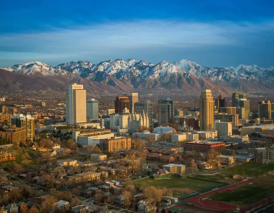 Salt Lake City skyline with snow-capped mountains in the background under a blue sky.