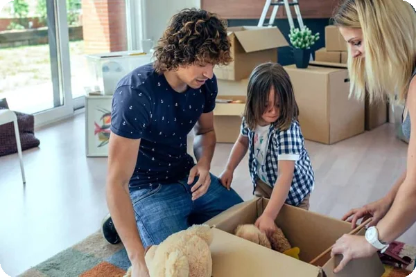 Parents help their young child put some of their toys into a cardboard box