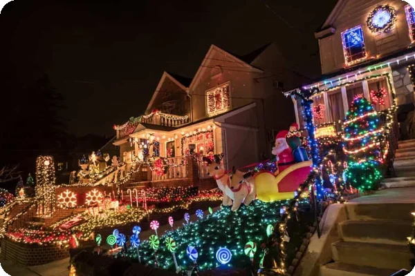 Brightly lit houses with extensive Christmas decorations including Santa, reindeer, trees, and glowing lollipops at night.