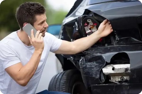 Man calling insurance after a car accident with visible damage.