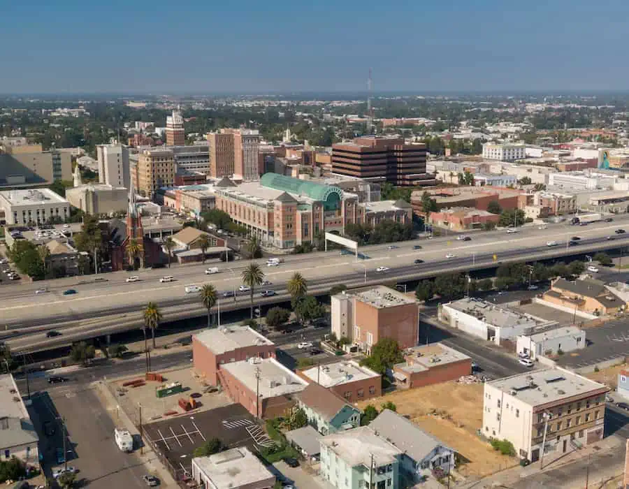 Aerial view of Stockton, California, USA, showcasing the city’s architecture, including office buildings, a church, and a shopping mall, alongside a busy highway with cars.