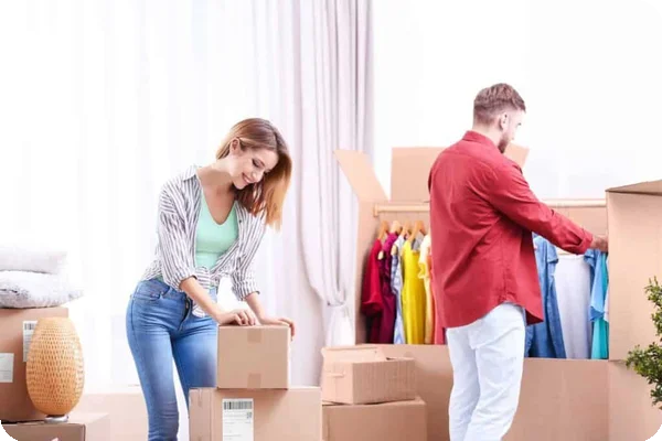 A couple works on packing boxes. One half makes sure the hangers in the wardrobe box are evenly spaced