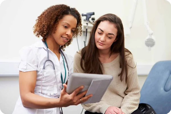 Female doctor with stethoscope shows a tablet to a female patient in an examination room