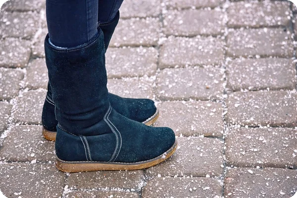 Dark boots on a paver path with scattered white granules, likely salt or sand.