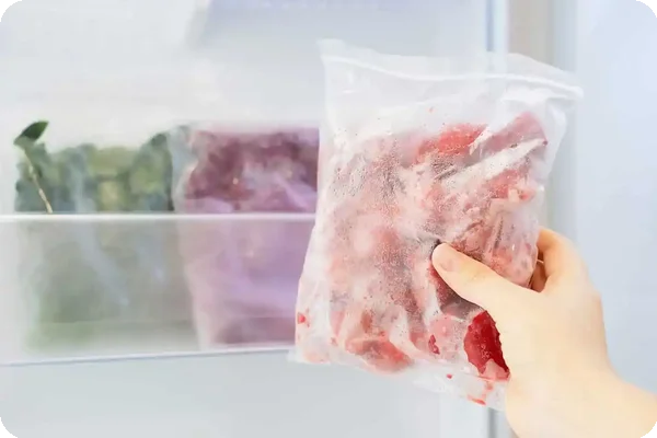 Hand holding a frozen bag of meat taken from a freezer.