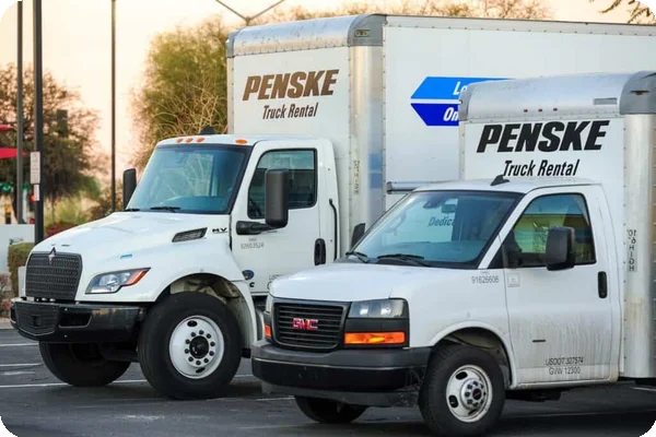 Two white Penske rental cargo trucks parked in a lot, displaying the brand's name and logo