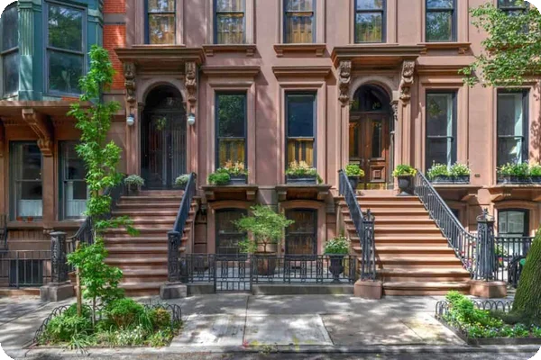 Row of brownstone buildings with front stoops, ornate railings, and street trees.