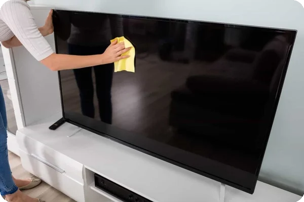 A person cleans the screen of a large flatscreen tv with a yellow microfiber cloth