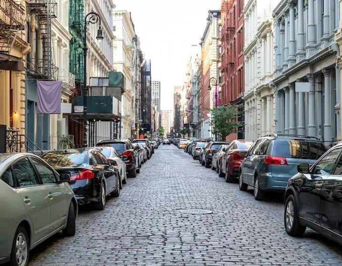 A view of a street in Manhattan, New York with cars parked on either side, leaving a narrow space between them