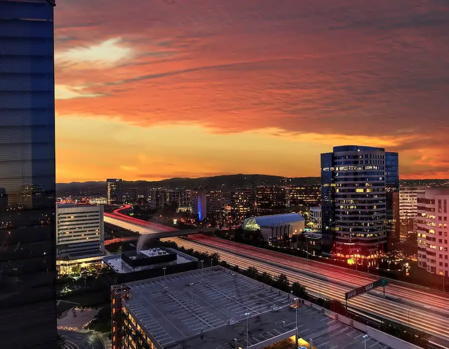 Sunrise over light trails and city lights on a highway in Irvine, California, USA.