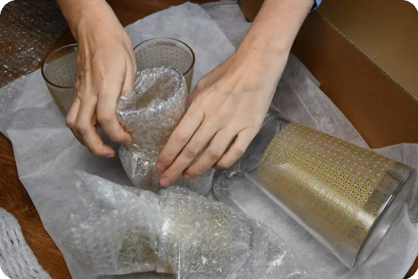 A person wraps a glass in bubble wrap