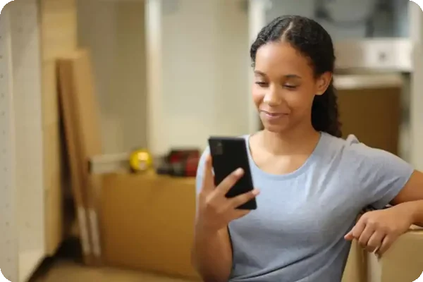 Woman checking best moving apps on phone while preparing for a move with boxes around her