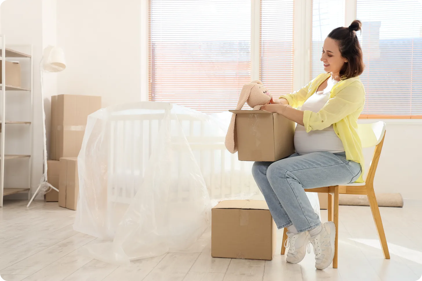A young pregnant woman takes a toy from a box in a child's bedroom on moving day