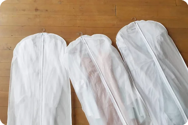 clothes in garment bags are laid out on a wooden floor