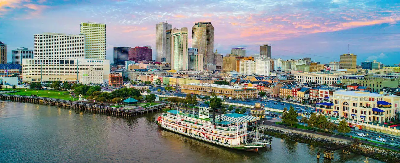 A view of New Orleans, LA's downtown skyline at sunset. There's a large part of the Mississippi River visible as well. 