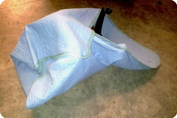 An image of an office chair wrapped in a moving blanket with one corner remaining, just as the instructions say