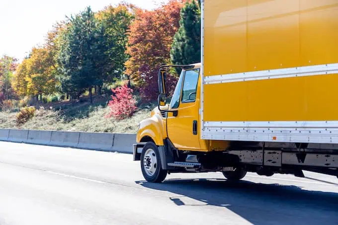 A yellow moving truck driving down the highway