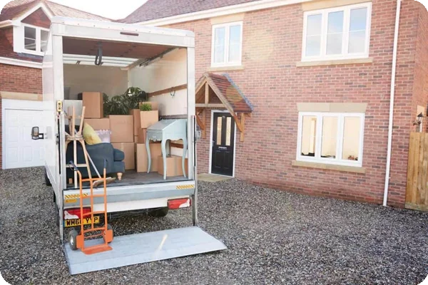 A moving truck full of furniture and boxes is parked outside of a brick home
