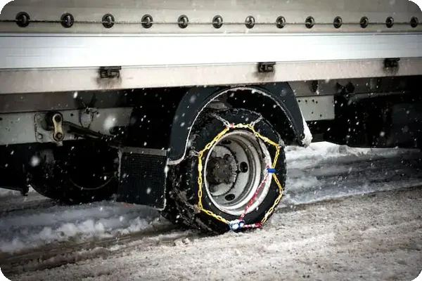 Close-up of snow chains installed on a rental truck tire for safe winter driving.