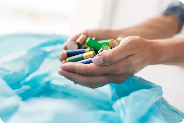 Cupped hands hold a mix of colorful AA, AAA, and button cell batteries over a blue bag.