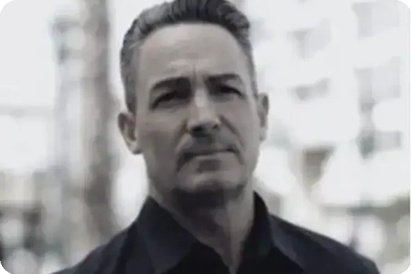 Bust-level portrait of a man with short, styled grey hair and a dark collared shirt, looking forward