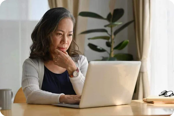 An older woman looks at her laptop thoughtfully as she searches for something on the internet