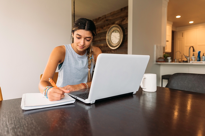 Women sitting with laptop writing on paper