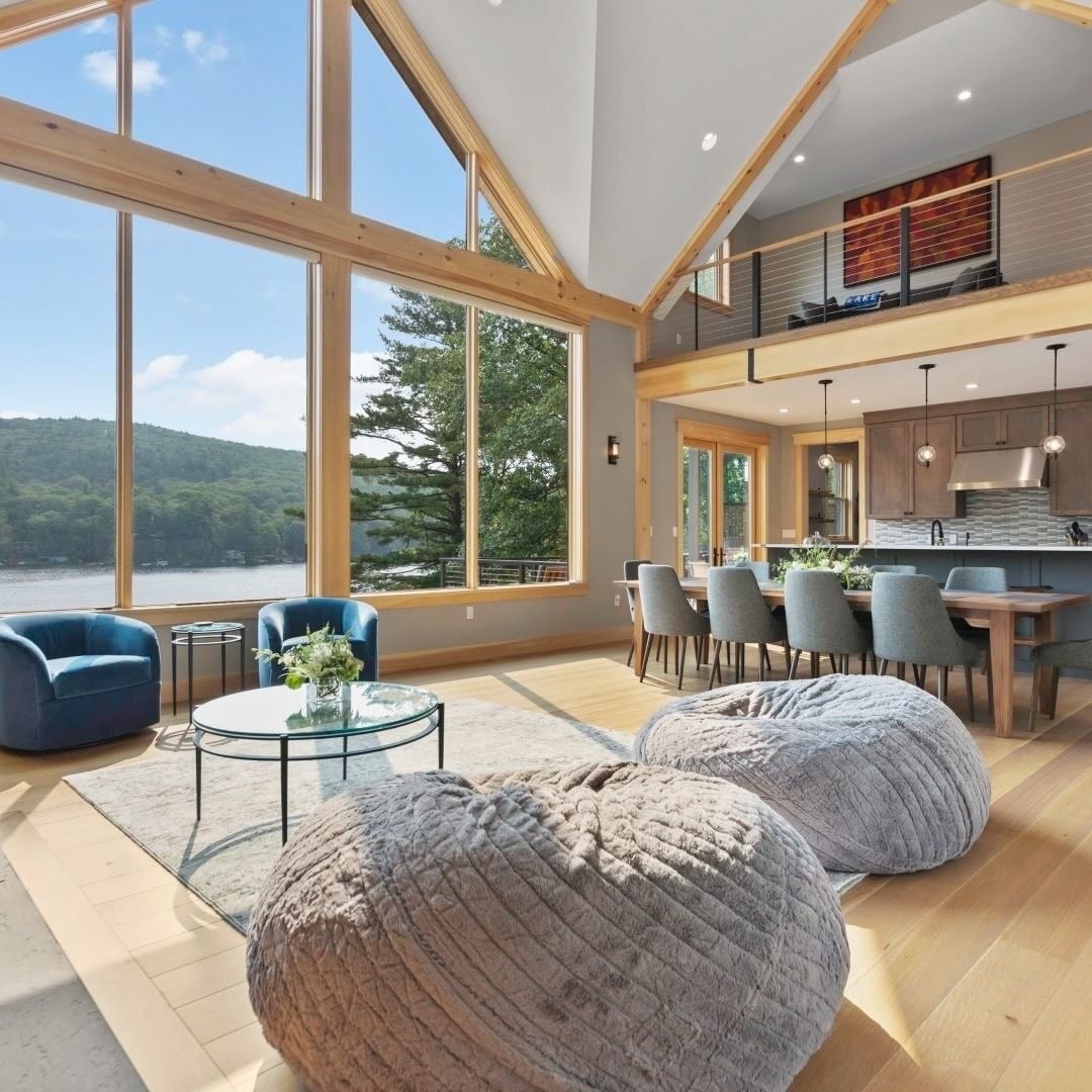 A living room with tall ceilings features triangle windows that form an entire window wall overlooking water.