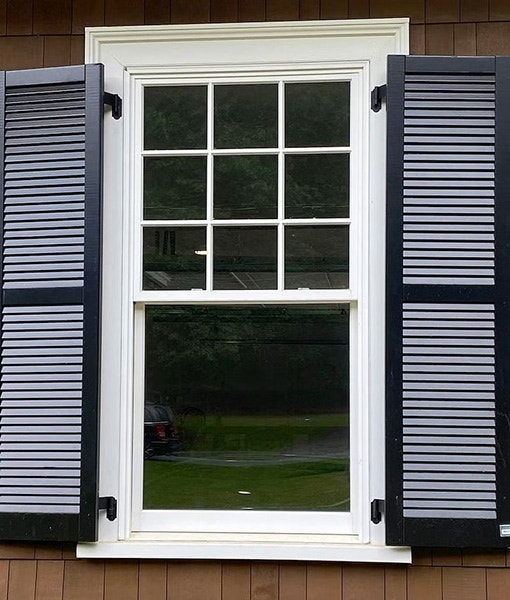 Craftsman-style historic double-hung window, complete with dark hinged shutters on each side.