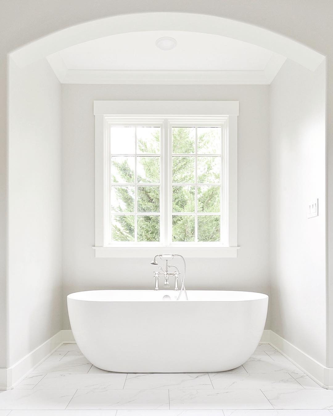 White on white bathroom with large casement window over freestanding tub