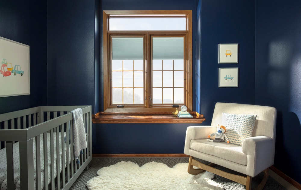 Baby nursery with navy walls, gray crib, and wood stained window with traditional grille pattern