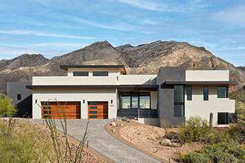 A contemporary home in the southwestern mountains with two orangish garage doors and high altitude glass for energy efficiency.