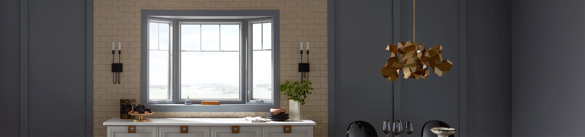 A modern kitchen featuring a bow window, gray walls, and decorative lighting, with a stylish countertop setup.