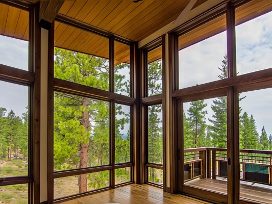 Floor-To-Ceiling Windows For Mountain-Side Living Room Two walls of glass made up of wood stained windows meet in the corner