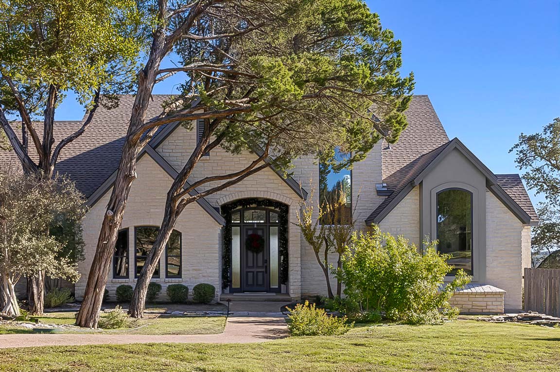 Beautiful stone house exterior with arched doorway and mature trees in front yard.