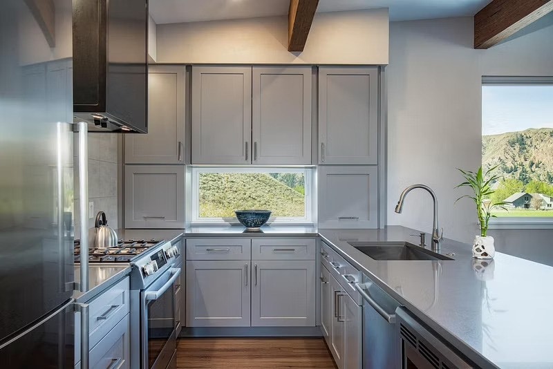 A white awning window is set in the middle of a wall of gray cabinets on the back wall of this kitchen.