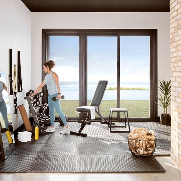 Woman in an in-home gym with black sliding patio doors and an ocean view