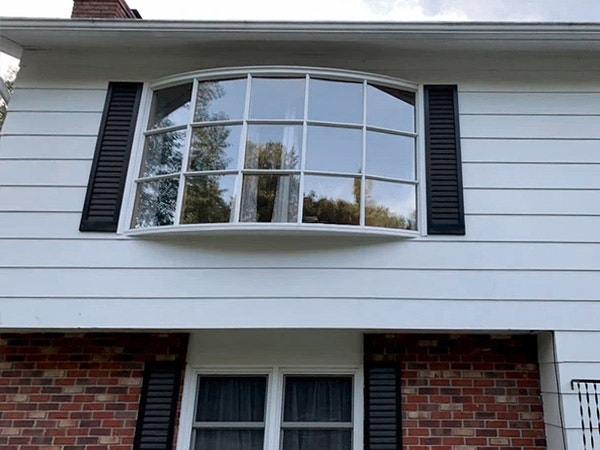 Before bow window on a house with white siding and brick.