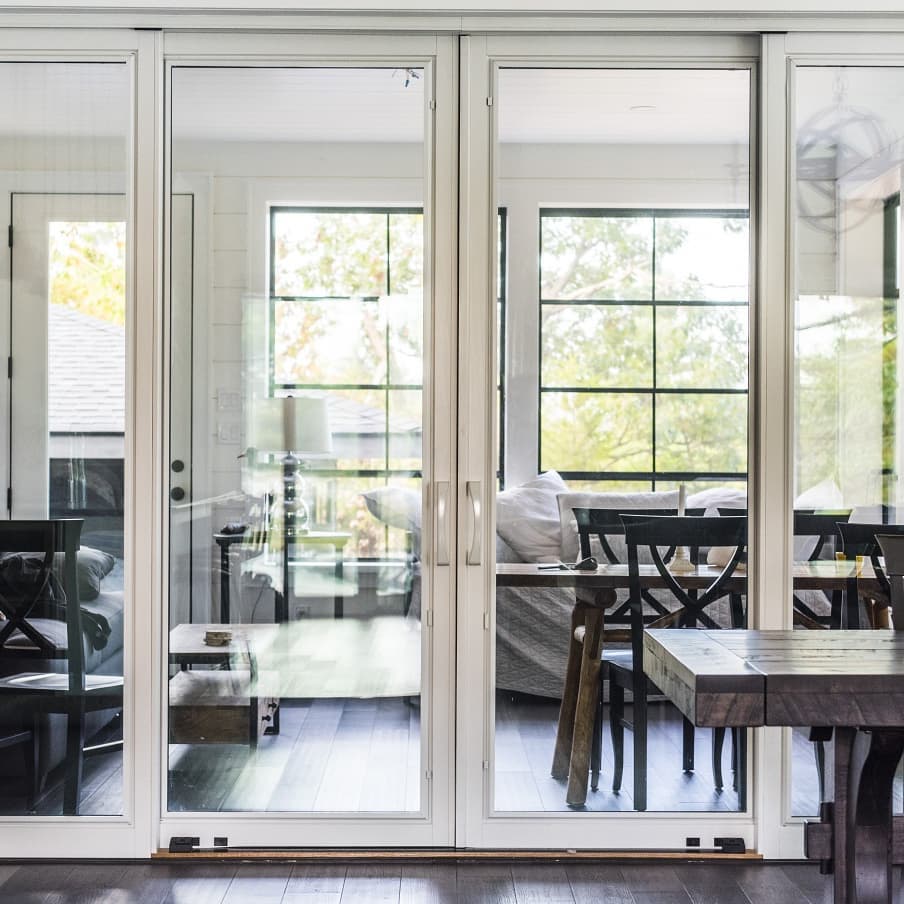 Sliding patio door with minimal white frame and large expanse of glass separates dining room from backyard